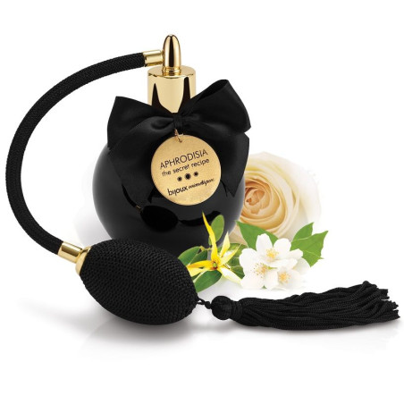Frasco negro de la bruma corporal Aphrodisia de Bijoux Indiscrets con vaporizador de perilla, lazo y borla, junto a rosa y jazmí